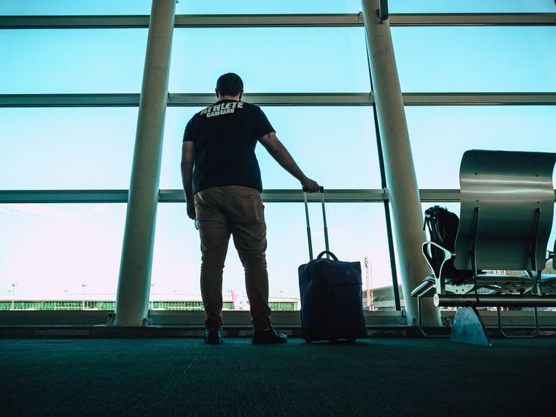Traveller with a wheeled cabin case looking out over the runway from an airport departure lounge