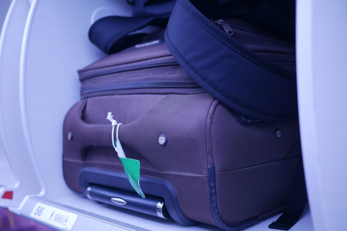 Purple soft cabin suitcase stowed in an open aeroplane overhead locker
