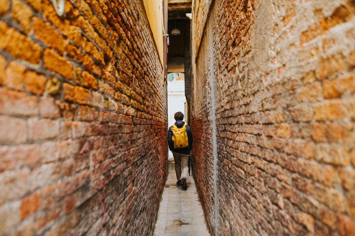 Traveller with a yellow backpack walking down a narrow brick alleyway in an old European city