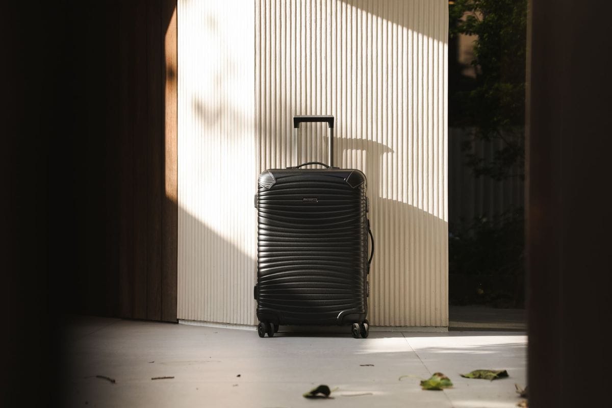 Black hard-shell spinner suitcase with its handle extended, standing against a sunlit wall