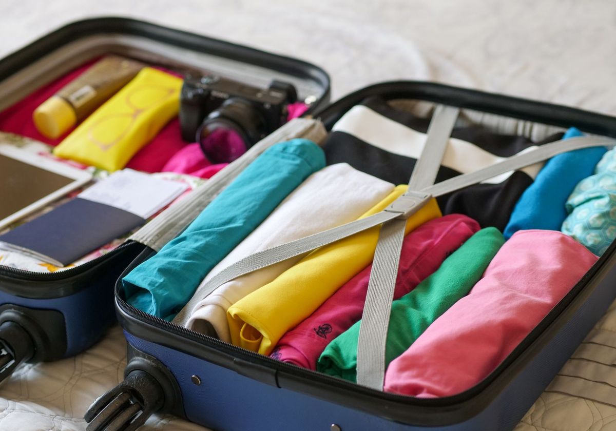 Open blue suitcase on a bed packed with rolled clothes, a camera and toiletries
