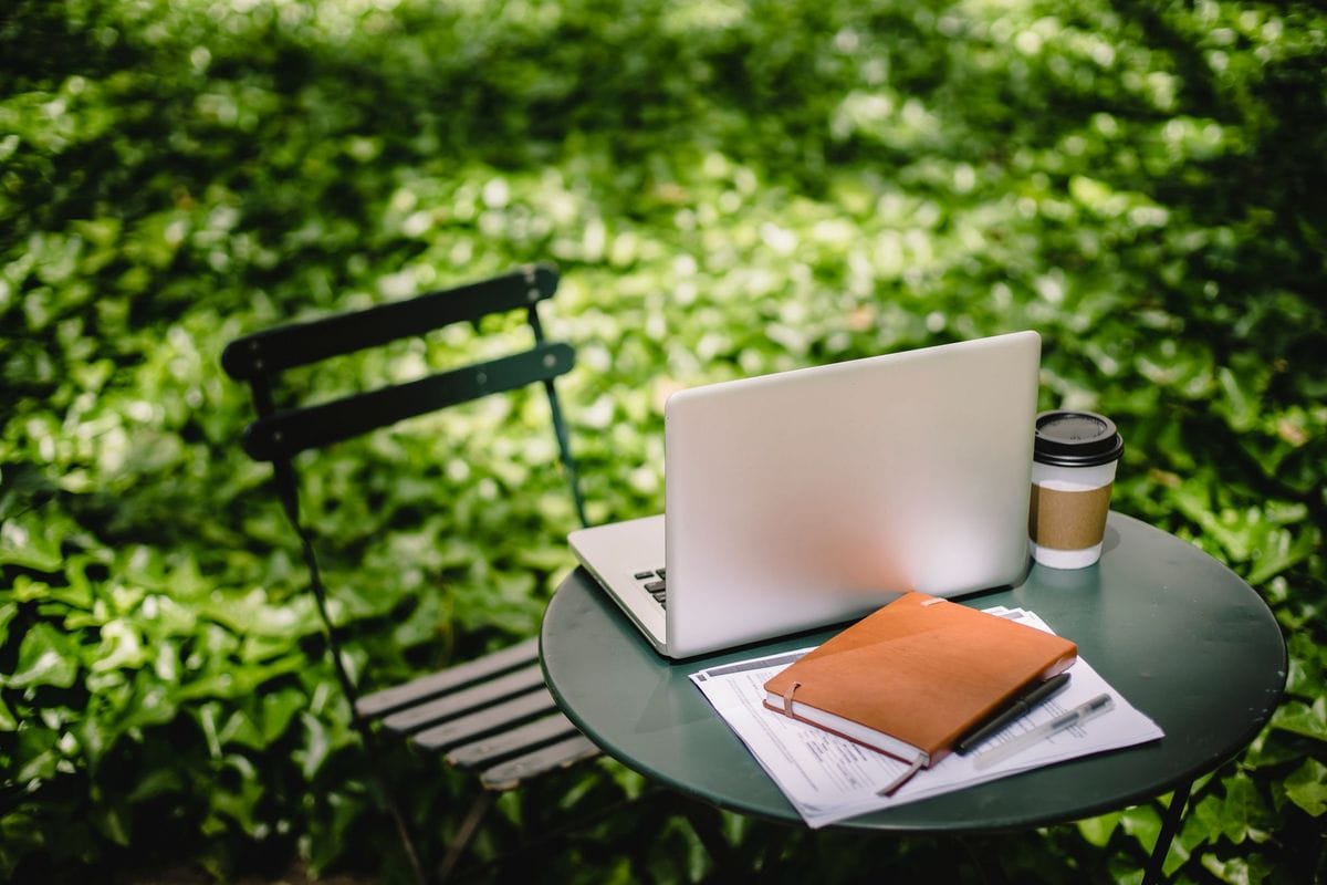 Laptop, notebook and takeaway coffee on a small round table in a leafy garden