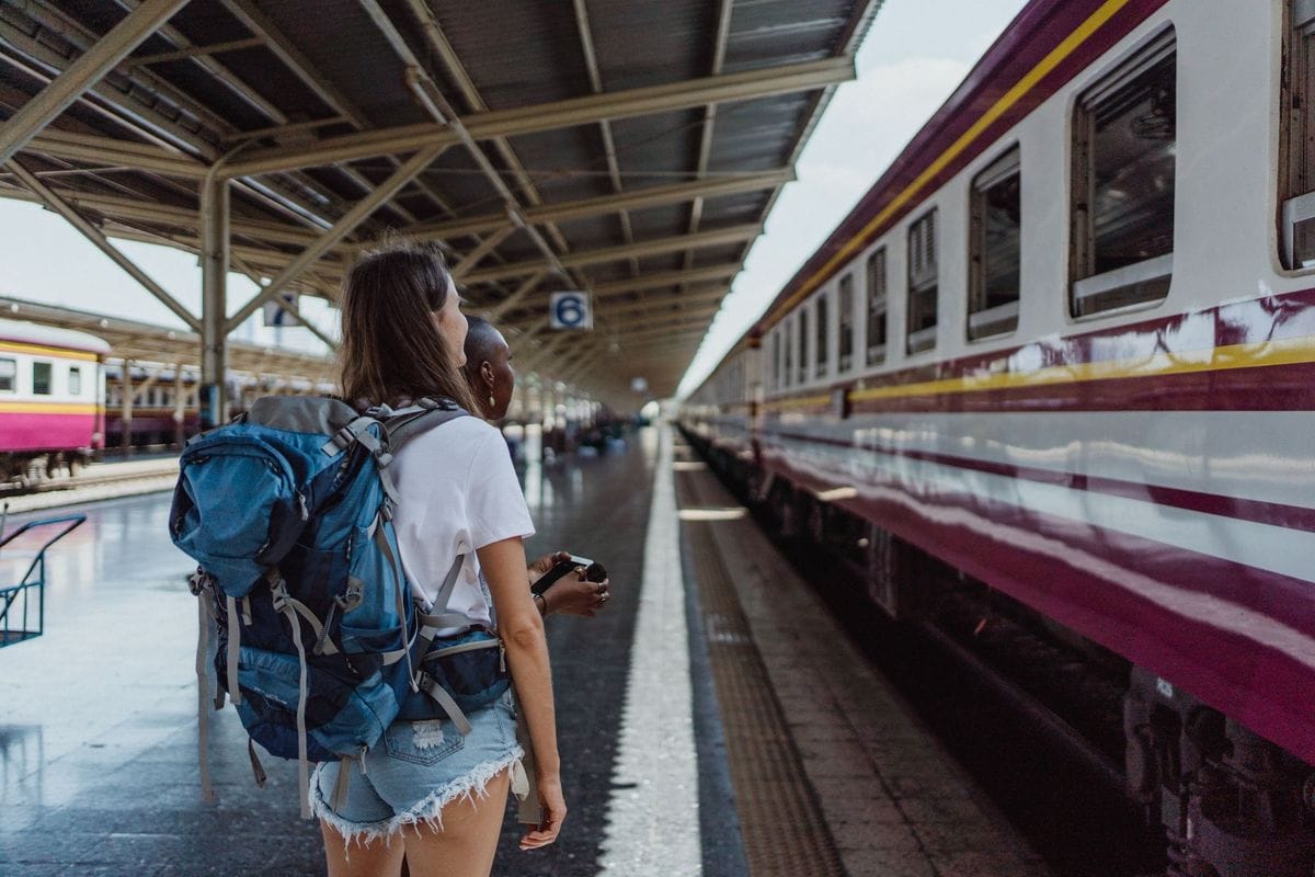 Woman with a large blue backpack waiting on a railway platform beside a train