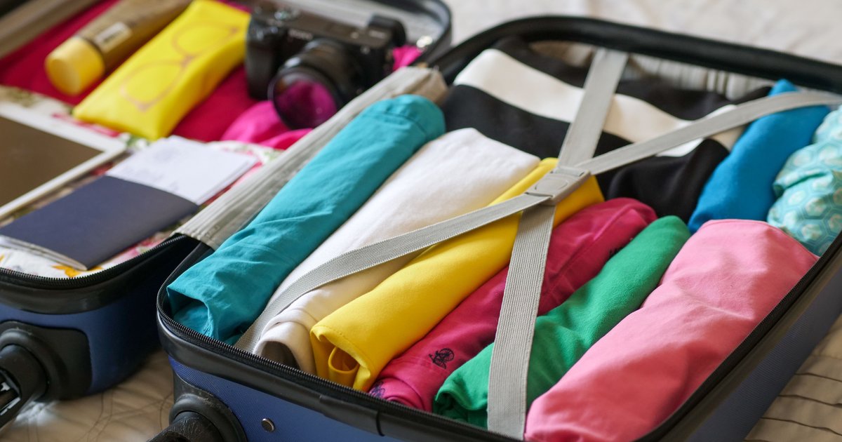 Open suitcase being packed with neatly rolled clothes on a bed