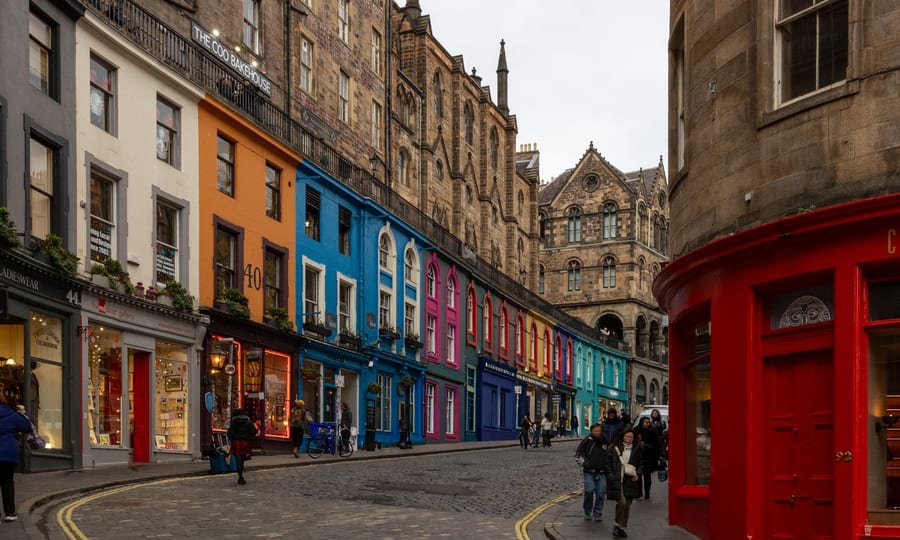 Colourful shopfronts along the curving cobbled Victoria Street in Edinburgh on a grey day
