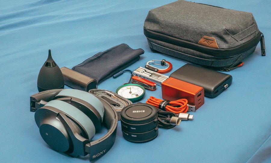Travel tech essentials laid out: power bank, GaN charger, universal adapter, headphones