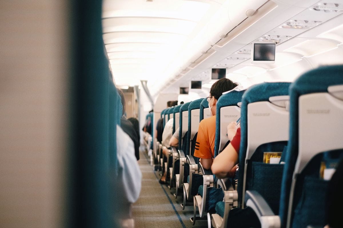 View down the aisle of a passenger aircraft between rows of blue seats with passengers seated