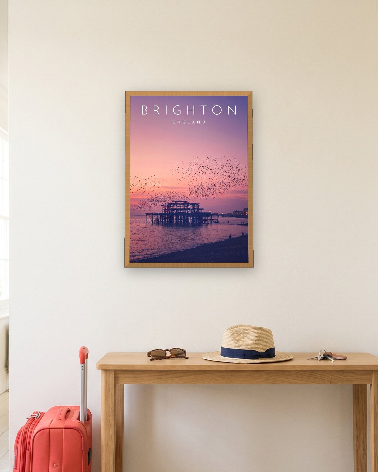 Brighton West Pier at Sunset print, natural oak frame A3 in a hallway with a packed suitcase
