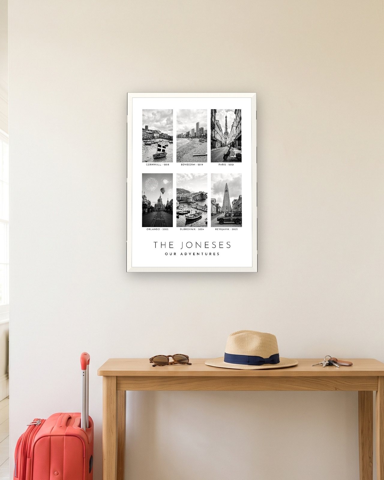 Our Family Adventures print in a white A3 frame in a hallway with a packed suitcase, six trips for The Joneses