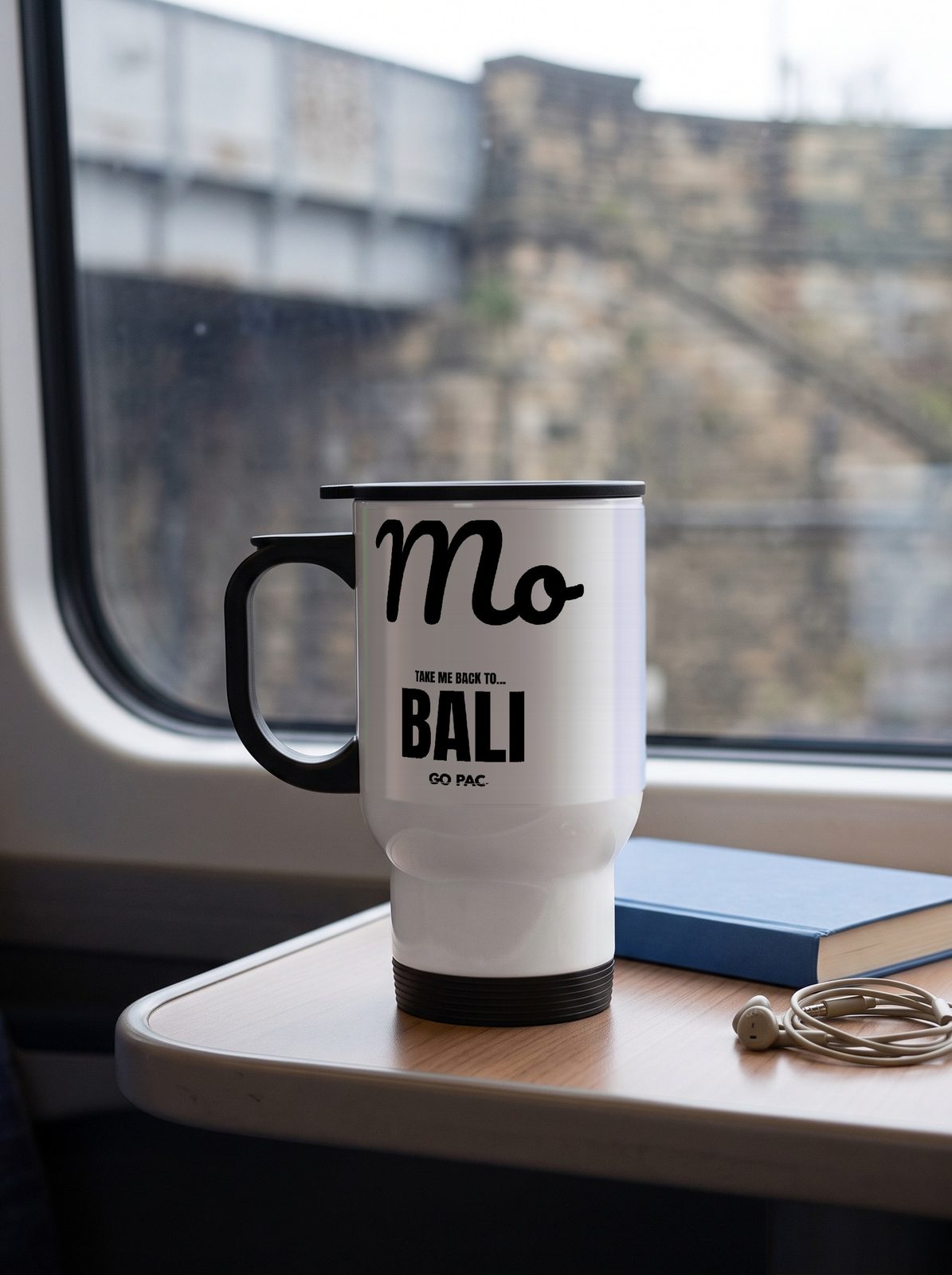White steel travel mug with Mo in black script and TAKE ME BACK TO... BALI, on a train table