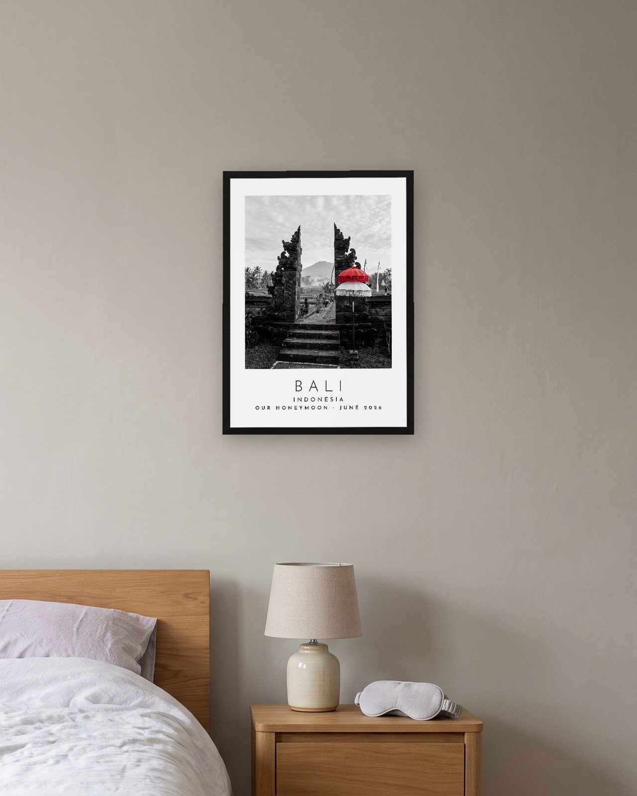 Our Trip Bali print: black frame A3 above a bedside table, personalised OUR HONEYMOON · JUNE 2026