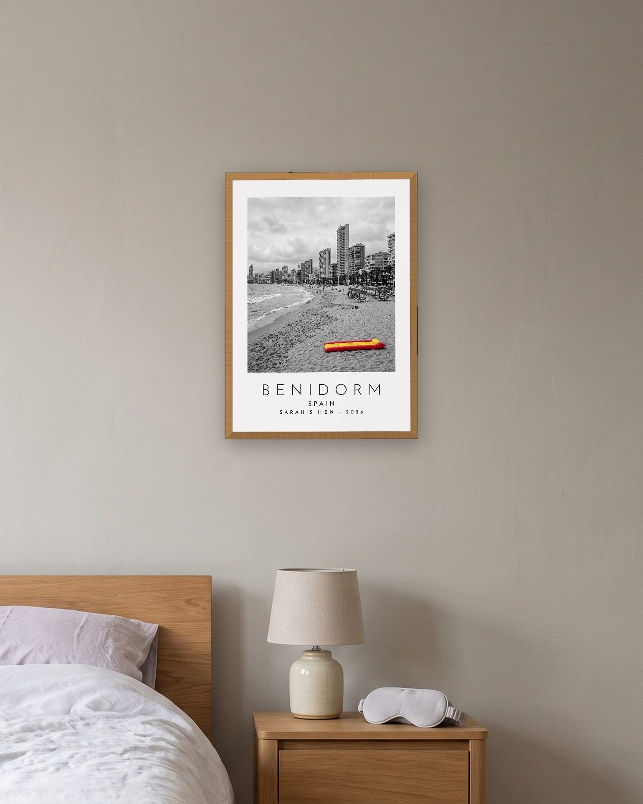 Our Trip Benidorm print: natural oak frame A3 above a bedside table, personalised SARAH'S HEN · 2026