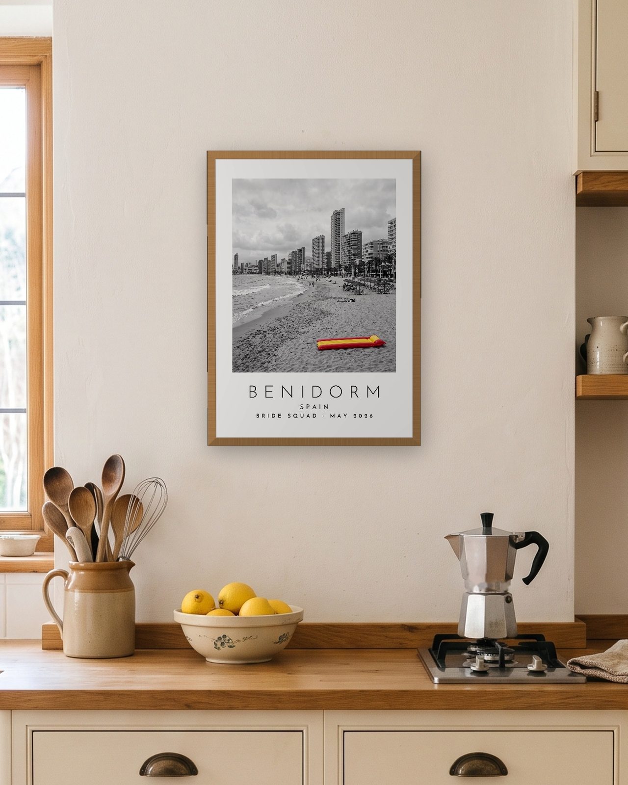 Our Trip Benidorm print: natural oak frame A3 in a bright kitchen, personalised BRIDE SQUAD · MAY 2026