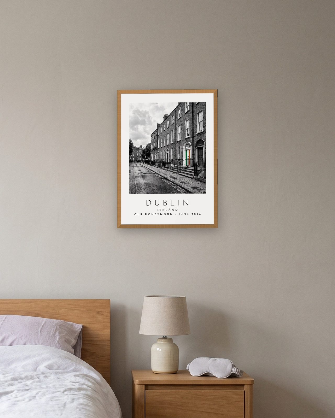 Our Trip Dublin print: natural oak frame A3 above a bedside table, personalised OUR HONEYMOON · JUNE 2026