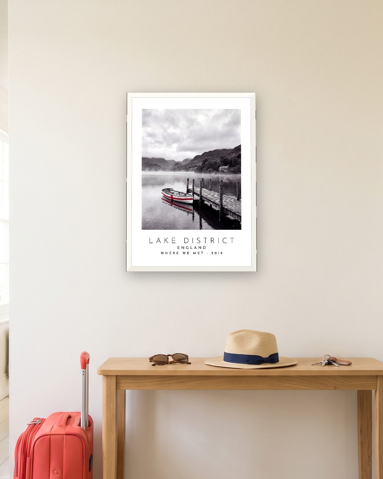 Our Trip Lake District print: white frame A3 in a hallway with a packed suitcase, personalised WHERE WE MET · 2019