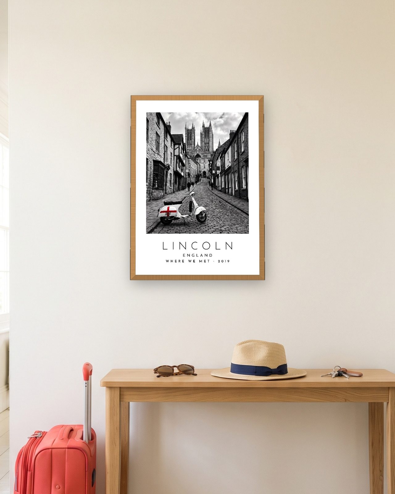 Our Trip Lincoln print: natural oak frame A3 in a hallway with a packed suitcase, personalised WHERE WE MET · 2019