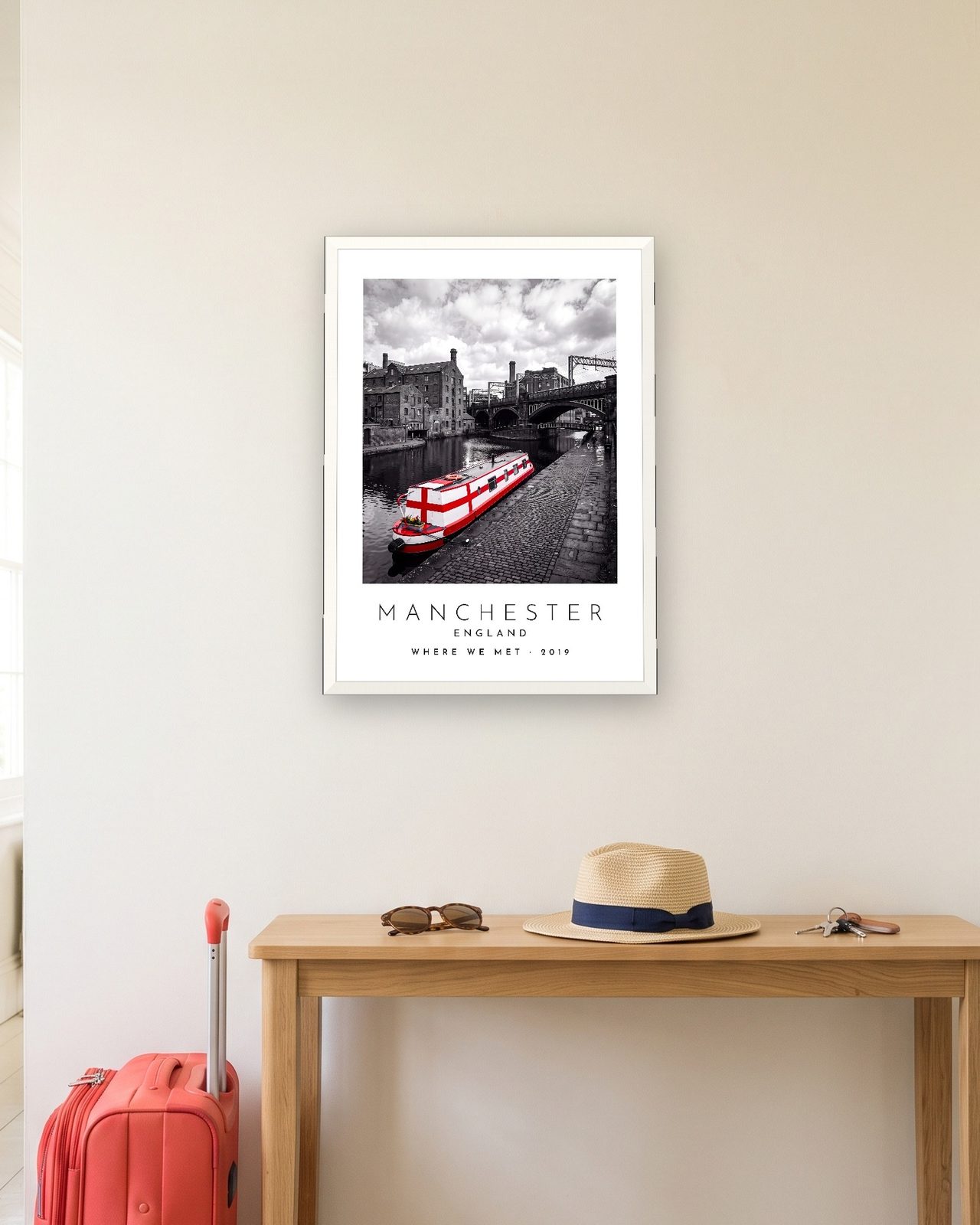 Our Trip Manchester print: white frame A3 in a hallway with a packed suitcase, personalised WHERE WE MET · 2019