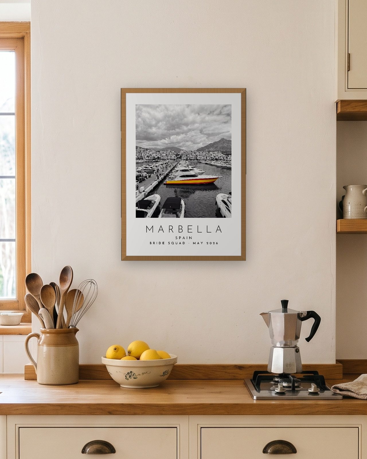 Our Trip Marbella print: natural oak frame A3 in a bright kitchen, personalised BRIDE SQUAD · MAY 2026