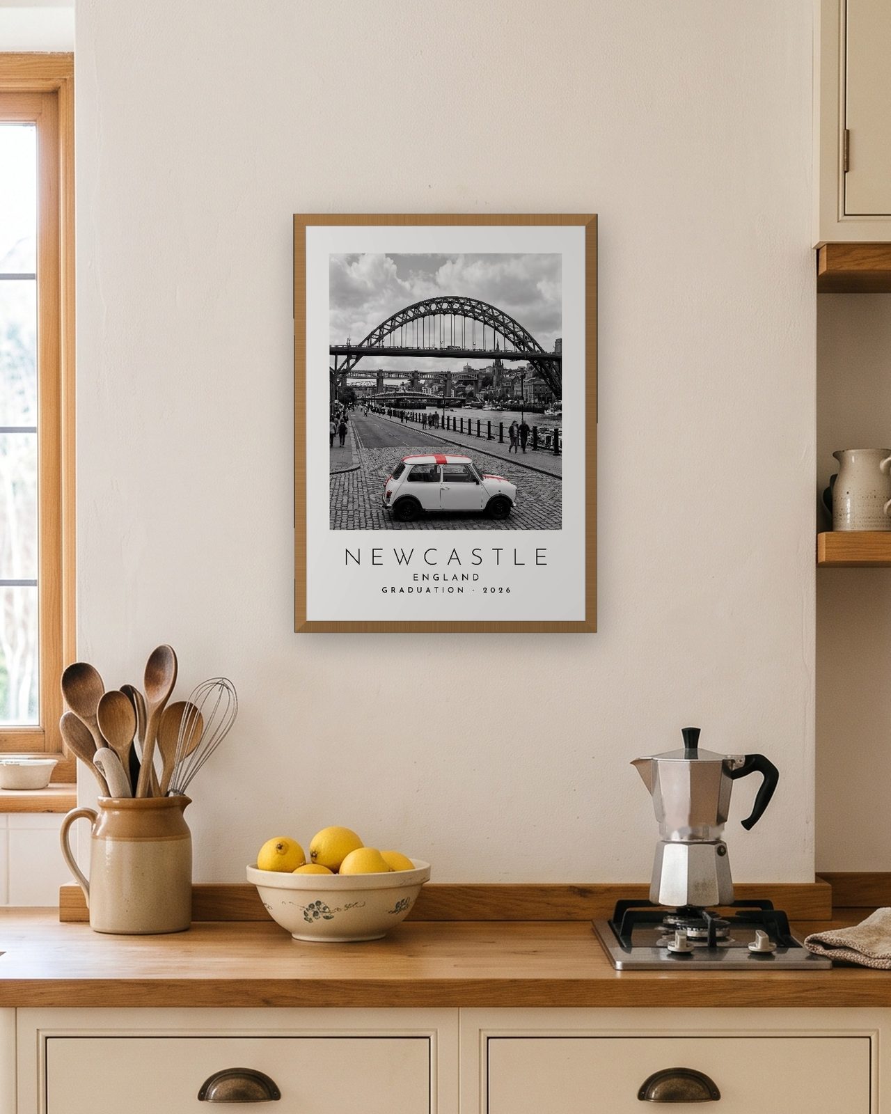 Our Trip Newcastle print: natural oak frame A3 in a bright kitchen, personalised GRADUATION · 2026