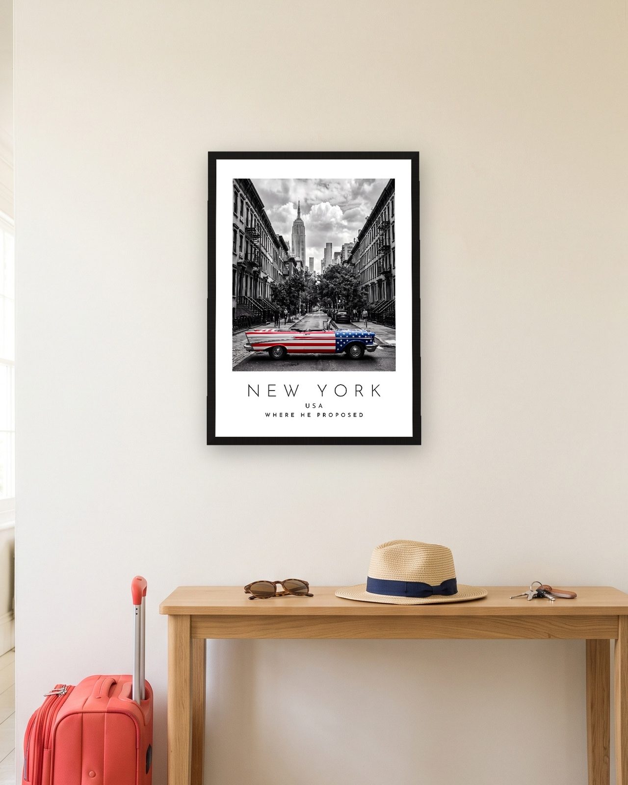 Our Trip New York print: black frame A3 in a hallway with a packed suitcase, personalised WHERE HE PROPOSED
