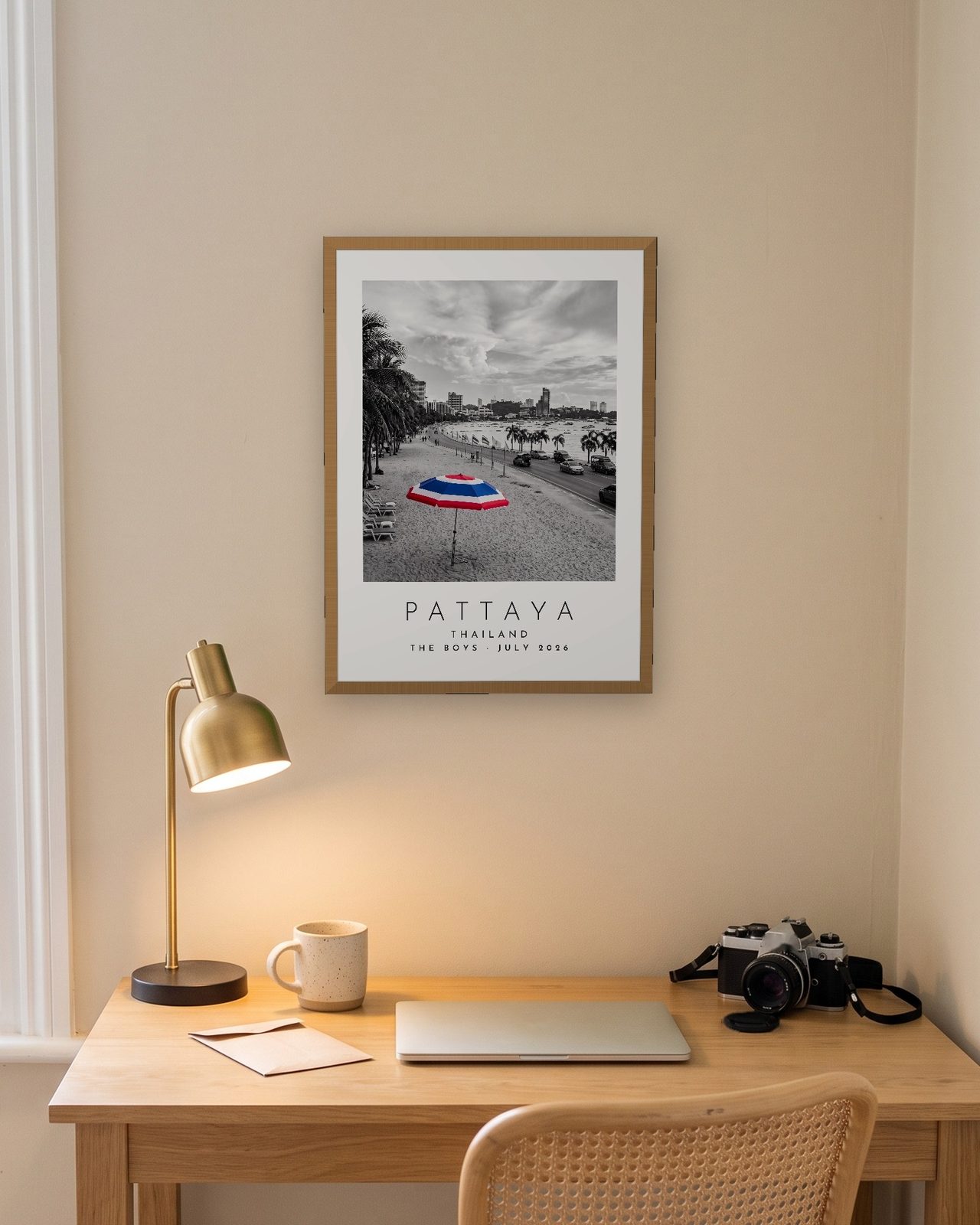Our Trip Pattaya print: natural oak frame A3 above a home office desk, personalised THE BOYS · JULY 2026