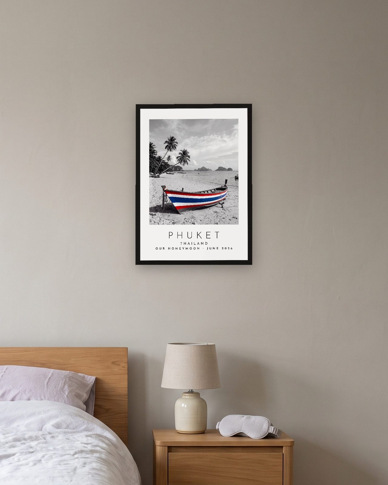 Our Trip Phuket print: black frame A3 above a bedside table, personalised OUR HONEYMOON · JUNE 2026