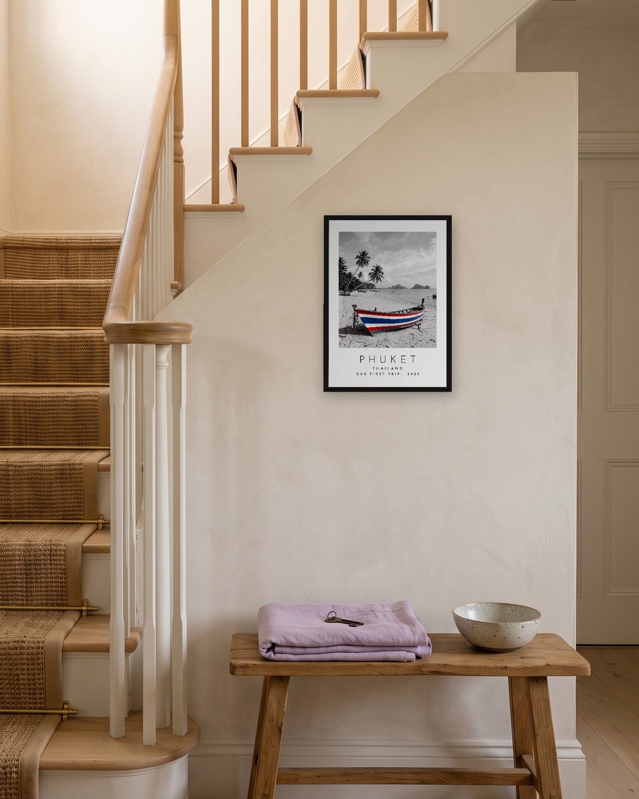Our Trip Phuket print: black frame A3 on a staircase wall, personalised OUR FIRST TRIP · 2023