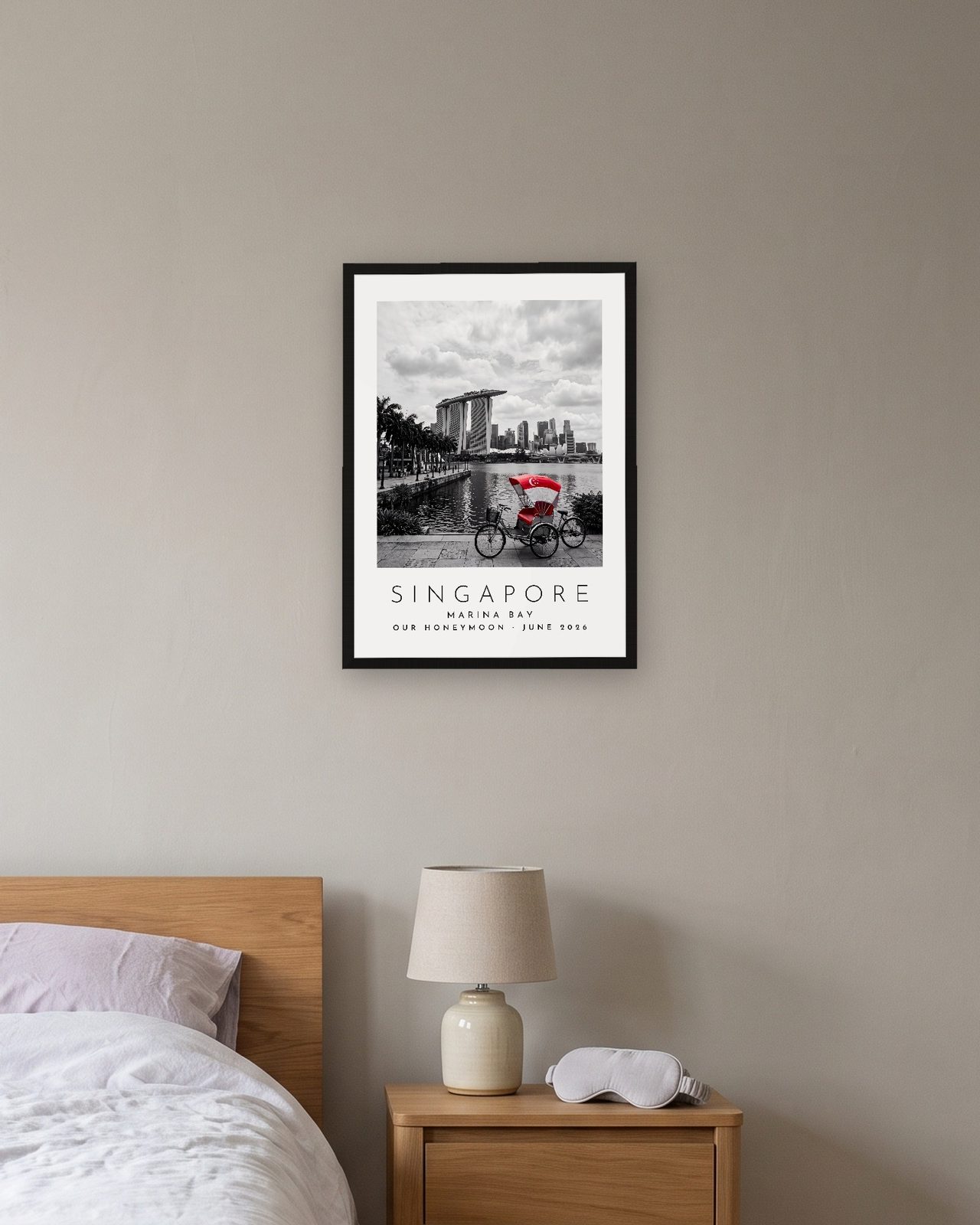 Our Trip Singapore print: black frame A3 above a bedside table, personalised OUR HONEYMOON · JUNE 2026